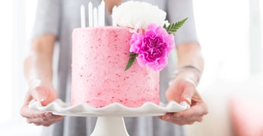 Person holding a tray with a pink layered cake with flower topping