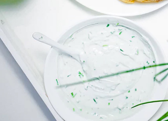 White food dip in a white bowl with white spoon, speckled with green herbs
