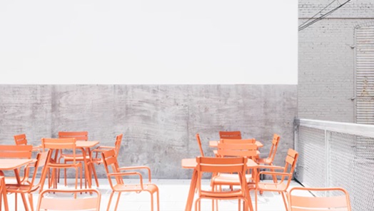 Industrial looking dining room with gray walls, furnished with wire frame orange tables and chairs